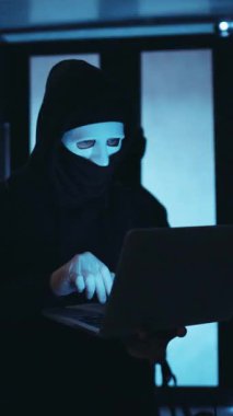 Gizemli bir kukuletalı figür son derece gelişmiş bir veri merkezinde parlak bir dizüstü bilgisayarda daktilo ediyor.