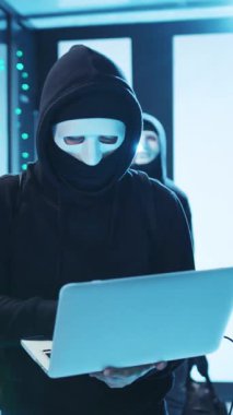 Maske takan gizemli bir kukuletalı şahıs, gelişmiş teknolojiyle dolu bir alanda dizüstü bilgisayarla karşılaşır.