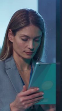 İş kıyafeti giymiş profesyonel bir kadın, modern işyeri dinamiklerini vurgulayan tabletine odaklanmış durumda.