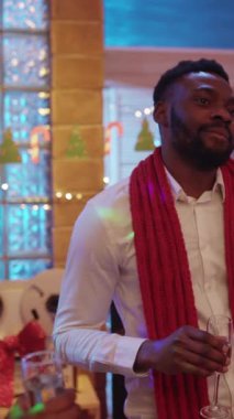 Kırmızı eşarplı neşeli bir adam şenlikli bir toplantıda kutlama yapar ve etrafındakilerle kadeh kaldırır.