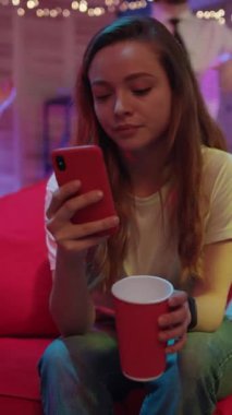 Etrafı canlı bir parti atmosferinde yakın arkadaşlarla çevriliyken derin bir yansımayla meşgul olan genç bir kadın.