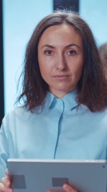 Uzun, dalgalı saçlı, parlak ve modern bir ortamda şık bir mavi gömlek giyen düşünceli bir kadın.