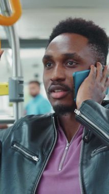 Derinden odaklanmış bir adam, şehirde metro trenine binerken önemli bir telefon görüşmesi yapıyor.