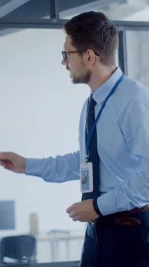 Mavi gömlekli ve kravatlı bir adam bir şirket ofisinde elinde kalemle dikiliyor ve düşünceli görünüyor.