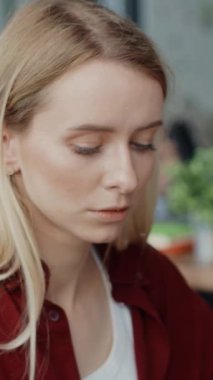 Sarı saçlı genç bir kadın, canlı bir kafede düşüncelere dalıp, samimi bir anı yakalıyor.