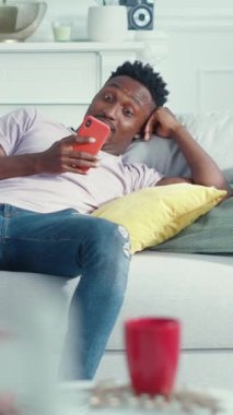 Modern bir adam rahat dairesinde uzanır, akıllı telefonunu kullanır ve rahat, bağlı bir yaşam tarzının tadını çıkarır.