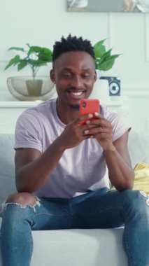 Mutlu ve neşeli genç bir adam, rahat ve modern bir iç mekanda akıllı telefonunu kullanma tecrübesinden zevk alıyor.