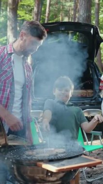 Bir aile mutlu bir şekilde dışarıda yemek pişirmekten ve ızgara etrafında resim gibi bir orman ortamında birlikte vakit geçirmekten hoşlanır.