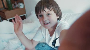 Tatlı, sevimli çocuk bir video kaydediyor, takipçilerine kendi tabletini gösteriyor. Yatakta çekim yapmak, küçük bir vlogger, yeni nesil. Eğlenceli, aktif bir yaşam tarzı..