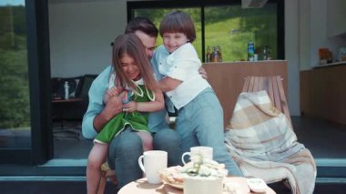 Yakışıklı bir baba güzel çocuklarını zevkle gıdıklıyor, sonra sarılıyorlar. Beraberlik, aile portresi. Pozitif duygular, iyi hissetmek. Açık havada çekim..