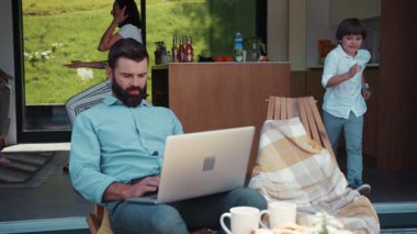 Yakışıklı sakallı iş adamı evde dizüstü bilgisayarla çalışıyor, sevgili küçük oğlu babasının yanına oturuyor, babası tatması için çocuğa meyve veriyor, tatlı karısı arka planda kızına bakıyor..