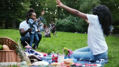 NEW YORK - 5 Nisan 2017: Kızı olan mutlu Afro-Amerikan çifti şehir parkında piknik yapıyor genç erkek ve çocuk dışarıda eğleniyor yavaş çekimde gülümsüyor yaz çocuğu doğası