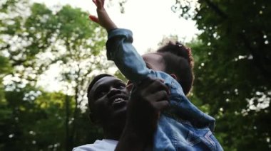 Afrikalı bir babanın kızına sarılıp el ele tutuşması tatilini parkta birlikte geçirmesi aile sevgisi gülümsemesi mutlu, yavaş çekim çocuk yaz çocuğu güneş kızı dışarıda ebeveynlik yapıyor