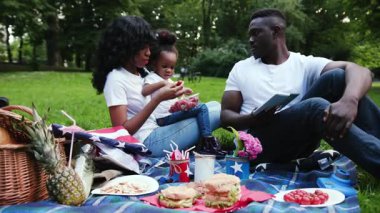 Yavaş çekim Afro-Amerikan çift kızı ile şehir parkında genç bir erkek ve çocuk piknik yapıyorlar. Çilek yiyorlar. Dışarıda eğleniyorlar.