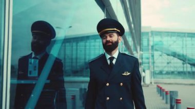 Olumlu gülümseyen sakallı pilot havaalanı terminalinin yanından geçiyor. Meslek konsepti, iyi günler, olumlu duygular. İyi hissediyorum. Erkek portresi