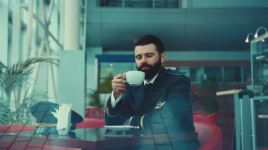 Yalnız yakışıklı pilot kafede oturur, kahve içer, mesajı alır, telefonunu kontrol eder ve neşeyle ona güler. Meslek konsepti, öğle yemeği, mola. Kalkışı bekliyorum. Erkek portresi