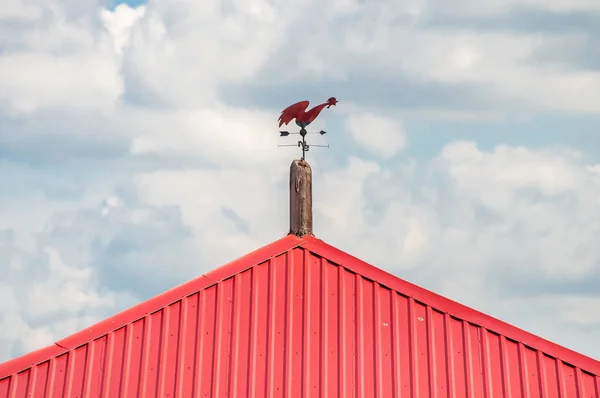 Shows the direction of the wind. Weathervane of a compass red cock on a red roof against the sky