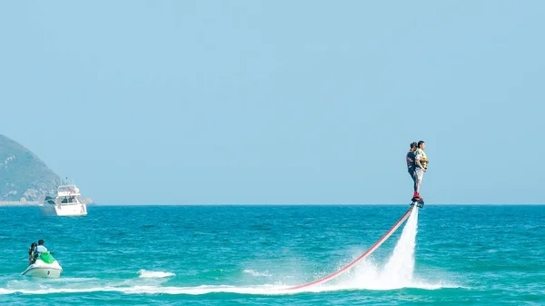 Hainan, Sanya, China - 14 de mayo de 2019: Flyboarding. Volando sobre el agua en el tablero con un potente chorro de agua. Atracción en la playa. Deportes extremos y recreación . — Foto de Stock