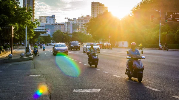 China, Hainan, Sanya - May 13, 2019: Road traffic on the background of the setting sun. Electric scooters - environmentally friendly transport. Glare on the photo, patch of reflected light, glitch. — Stock Photo, Image