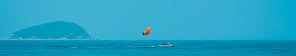 Parasailing is an active form of recreation. The man is towed on a boat and flies with a parachute over the water. Panorama