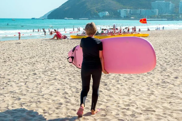 Surfing. Young girl with a surfboard goes on the beach. Extreme water sports. Healthy active lifestyle. Summer vacation.