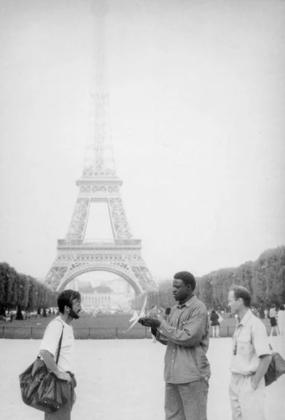 Paris, foto em preto e branco, agosto de 1994. Um vendedor de rua negra está tentando vender um avião de brinquedo para turistas ucranianos. No fundo Torre Eiffel . — Fotografia de Stock