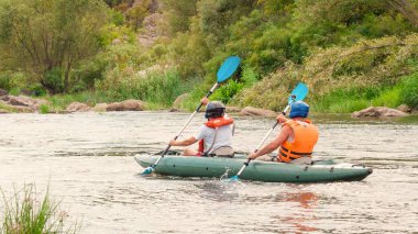 Rafting gezisi. İki kürekçi lastik şişme botla nehirde rafting ediyor. Arka görüş. Takım çalışması kavramı, sağlıklı yaşam tarzı.