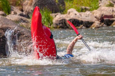 Oyun teknesi. Elinde küreklerle kayıkta oturan bir adam su üzerinde egzersiz yapar. Whitewater üzerinde serbest kayak. Eskimo rulo.