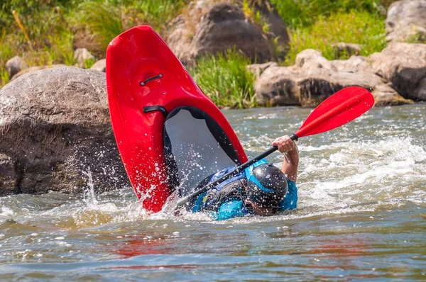 Playboating. A man sitting in a kayak with oars in his hands performs exercises on the water. Kayaking freestyle on whitewater. Eskimo roll.