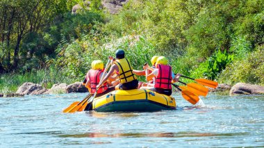Rafting gezisi. Bir grup kadın ve erkek nehirde büyük bir şişme bota iner..