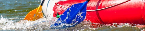 Rafting trip. Close up view of oars with splashes of water. Rowers make an effort to overcome the turbulent river. The concept of teamwork, healthy lifestyle.