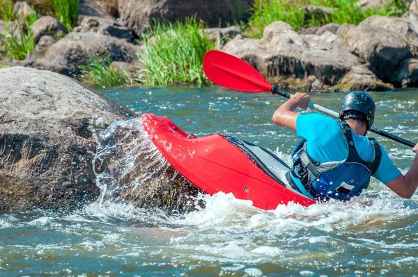 Playboating. A man sitting in a kayak with oars in his hands performs exercises on the water. Kayaking freestyle on whitewater. Eskimo roll.