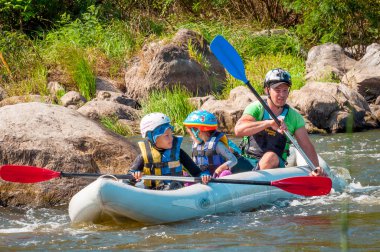 Myhiya, Ukrayna - 17 Ağustos 2019: Rafting. İki çocuklu bir baba nehirde şişme bir tekneye biner. İnsanların samimi duyguları. Mutlu aile konsepti.