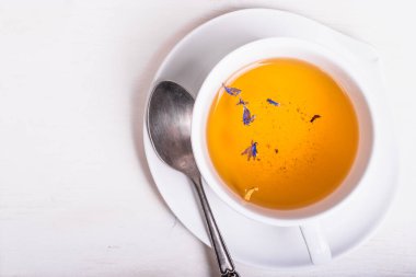 Bir fincan yeşil çay, çiçek yapraklı çay, çay tabağında kaşık, beyaz ahşap masa, üst manzara, kopyalama alanı.