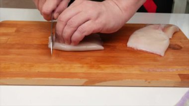 Bir adam ahşap mutfak tahtasına saplanmış bir bıçakla kalamar filetosunu kesiyor.