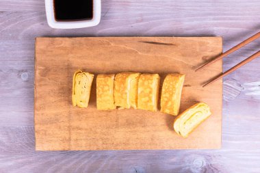 Tamago Japon omleti ve çay tabağında soya sosu, ahşap servis tahtasındaki çubuklar, yakın çekim, üst manzara.