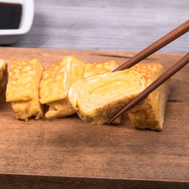 Tamago Japon omleti ahşap servis tahtasında ve yemek çubuklarında bir parça omlet, yakın plan.