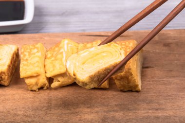 Tamago Japon omleti ahşap servis tahtasında ve yemek çubuklarında bir parça omlet, yakın plan.