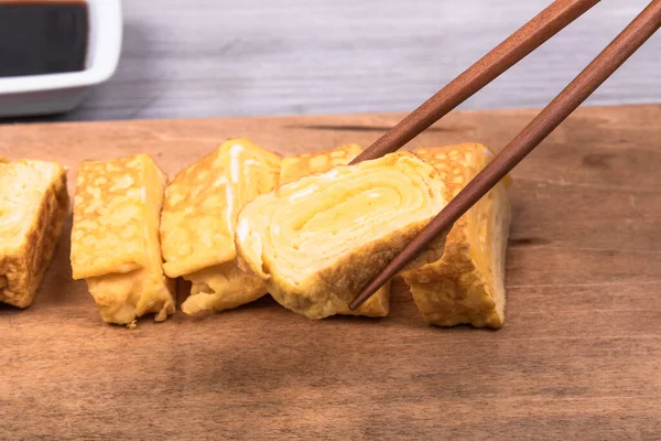 Tamago Japon omleti ahşap servis tahtasında ve yemek çubuklarında bir parça omlet, yakın plan.