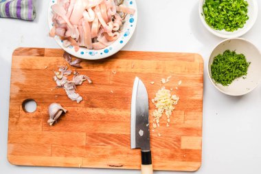 Kalamar sosu pişiriyorum. Santoku bıçağı ve doğranmış sarımsak mutfak ahşap kesme tahtasının üzerindeyken, doğranmış mürekkep balığı, dereotu ve maydanoz masanın yanında kaselerin içinde.