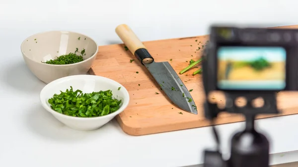 Shooting a video plot for a food blog, vlog - the camera takes pictures of products. Dill stalks and a santoku knife lie on a kitchen wooden cutting board