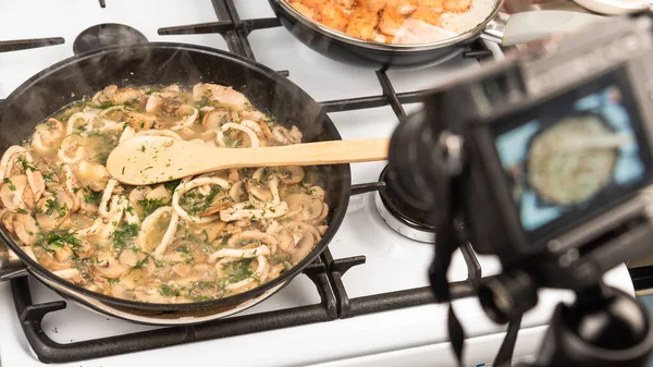 Shooting on the camera for food blog cooking creamy sauce with squid and mushrooms. Sliced squid rings and champignons, with dill and parsley stewed with cream in a pan