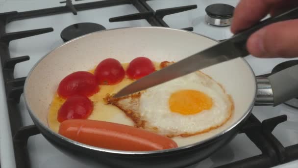 Petit déjeuner rapide - œufs, tomates et saucisses sont frits dans une poêle avec un revêtement antiadhésif blanc