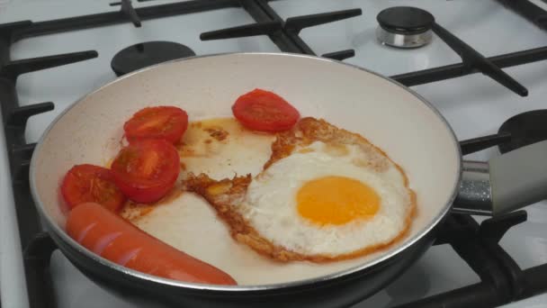Petit déjeuner rapide - œufs, tomates et saucisses sont frits dans une poêle avec un revêtement antiadhésif blanc