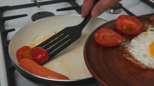 快速早餐 一个男人把一个鸡蛋和西红柿与香肠从一个煎锅放在盘子里 — 图库视频影像
