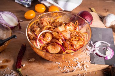 Cam bir kasede baharatlı biber sosunda soğanlı, sarımsaklı ve biberli tavuk parçaları ve ahşap bir masada güveç veya kızarmış tabak pişirmek için malzemeler. Doğulu, Hintli, Karayipli, Akdeniz yemekleri