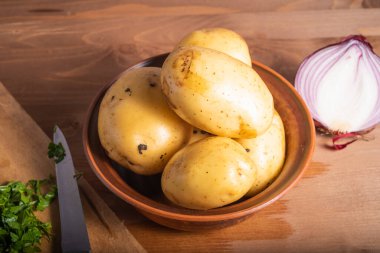 Vejetaryen güveci hazırlamak için gereken malzemeler. Kasede patates, yarım soğan, soğan ve doğranmış sebze.