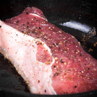 Biber ve tuz serpilmiş taze çiğ biftek bir tavada kızartılır. Yakın plan, makro.