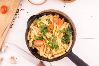 Domatesli basit İtalyan makarnası ve maydanozlu sarımsak. Hafif bir masada, içinde yemek malzemeleri olan maydanoz serpiştirilmiş.