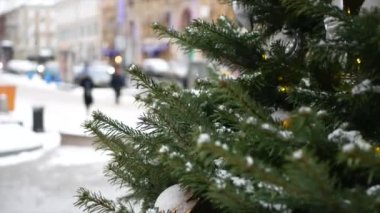 Üzerinde kar olan ladin dalları ve ön planda Noel oyuncakları ve arka planda kış sokağı.